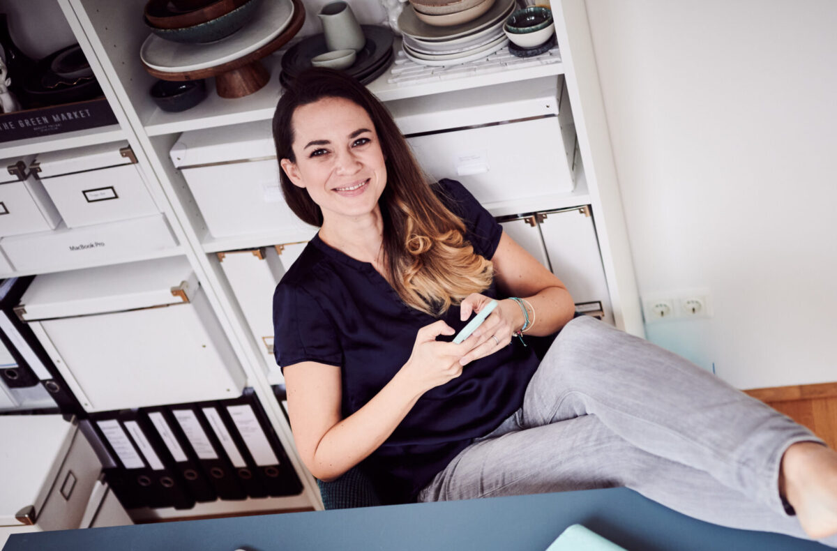 Mariella mit dem Smartphone in der Hand am Schreibtisch