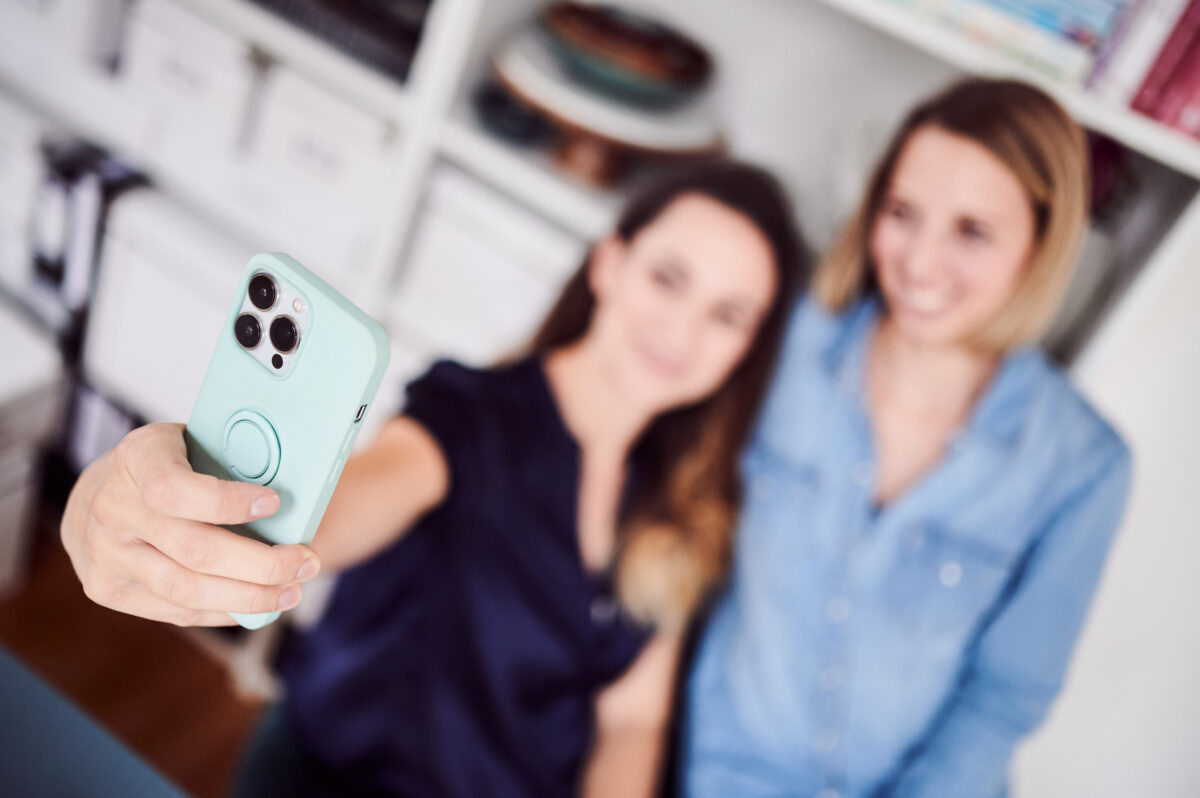 Smartphone im Vordergrund, zwei Frauen im Hintergrund