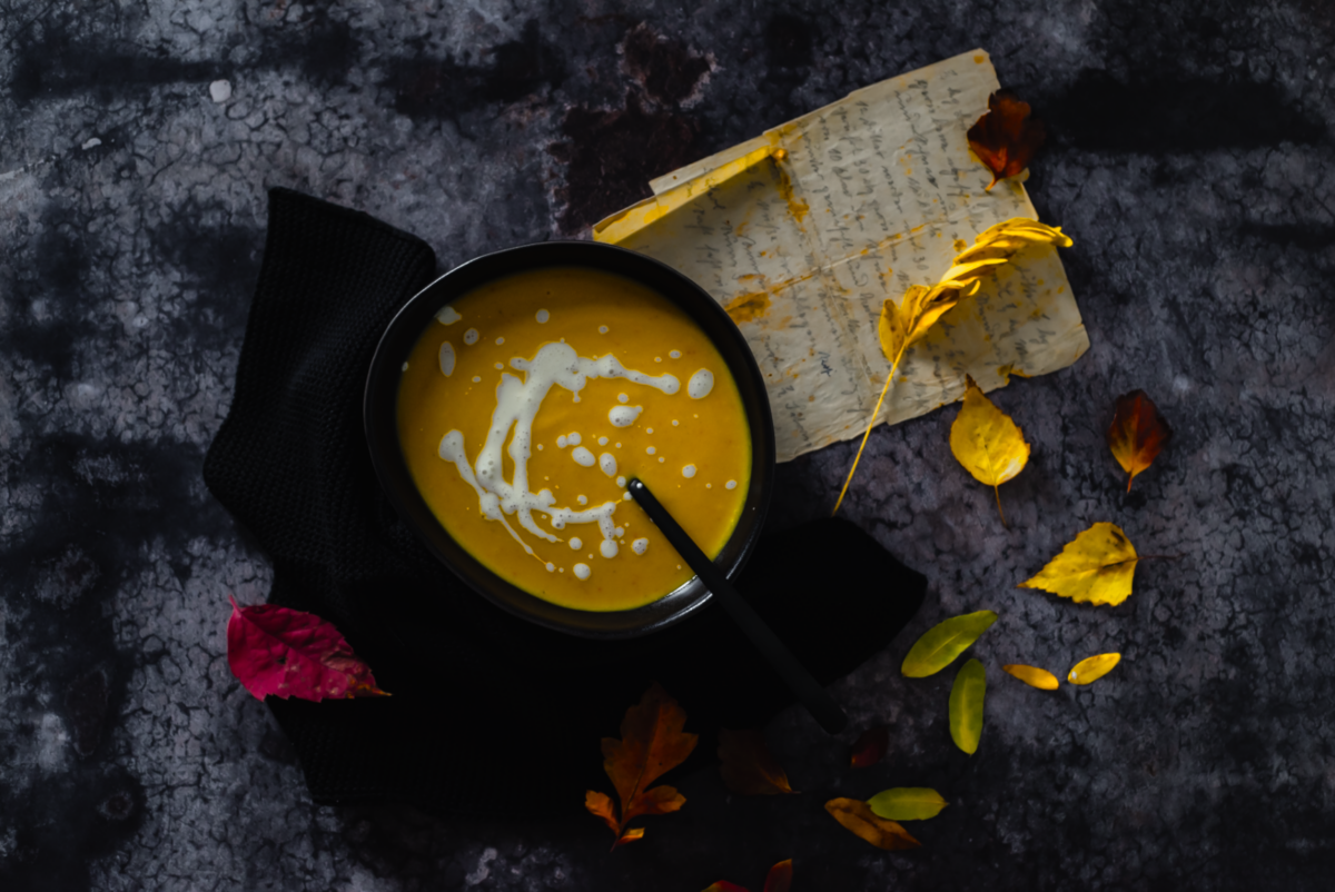 Herbstliche Kürbiscremesuppe mit Sahne und Blättern auf dunklem Untergrund