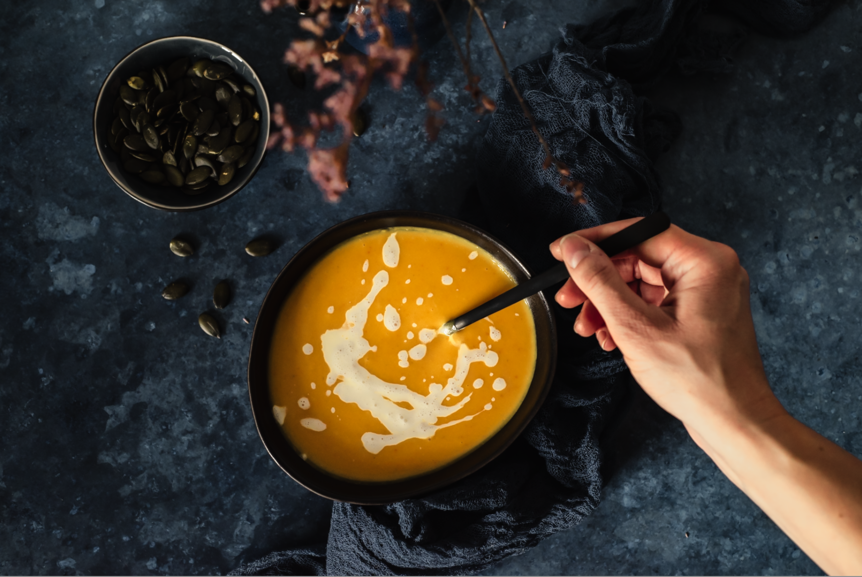 Kürbiscremesuppe auf dunklen Untergrund mit Löffel und Arm