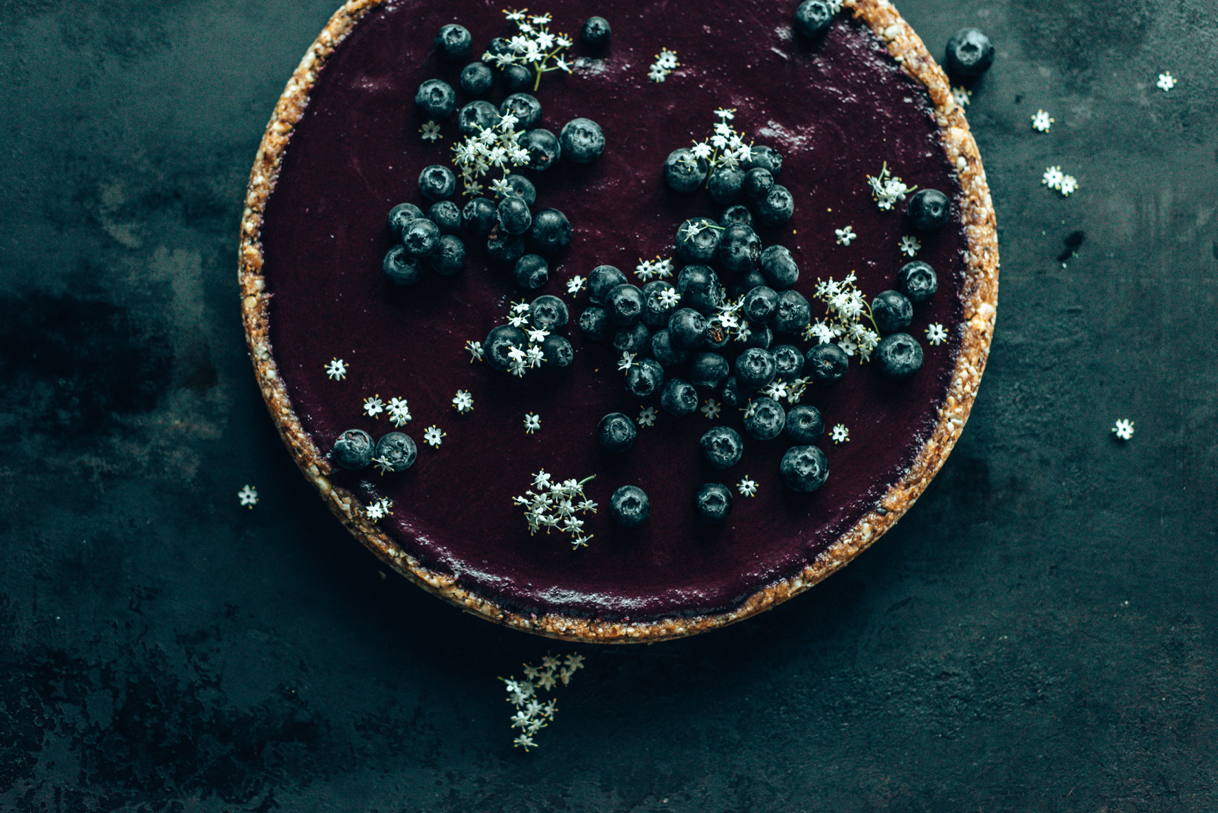 Heidelbeer-Tarte auf dunklem Untergrund mit Holunderblüten